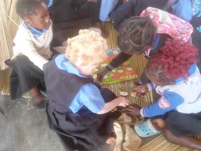 Several schoolchildren, including one child with albinism, sit on a mat and play a board game together